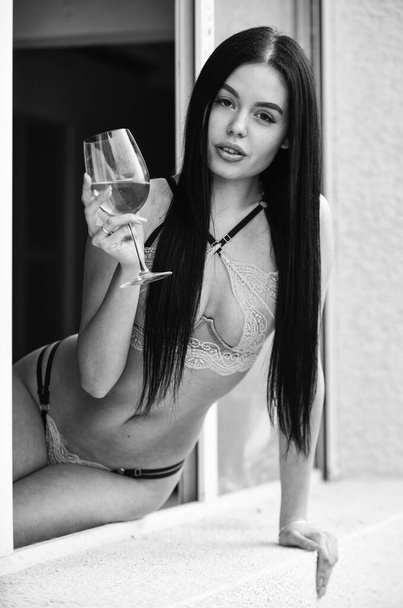 Сексуальна дівчина з алкогольним коктейлем. Сексуальна дівчина з келихом вина. Домашня вечірка. Елітне вино. Вона багато знає про задоволення. Концепція гедонізму. Гаряча леді в еротичній білизні сидить підвіконня. Жінка п'є вино
 - Фото, зображення