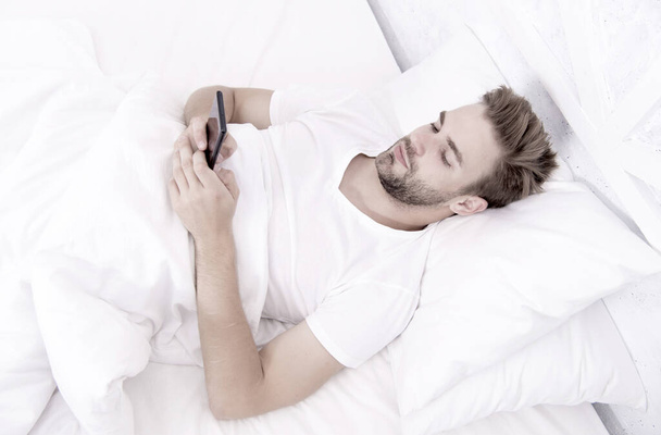 Application analyzes stages of sleep and wakes you up at optimal time. Provide deeper sleep analysis. Set up morning alarm. Apps that help monitor sleep. Man use mobile phone in bed. Waking up - Φωτογραφία, εικόνα