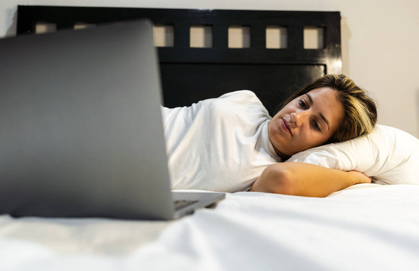 młoda Latynoska kobieta leży w łóżku i ogląda swój ulubiony serial na laptopie - Zdjęcie, obraz