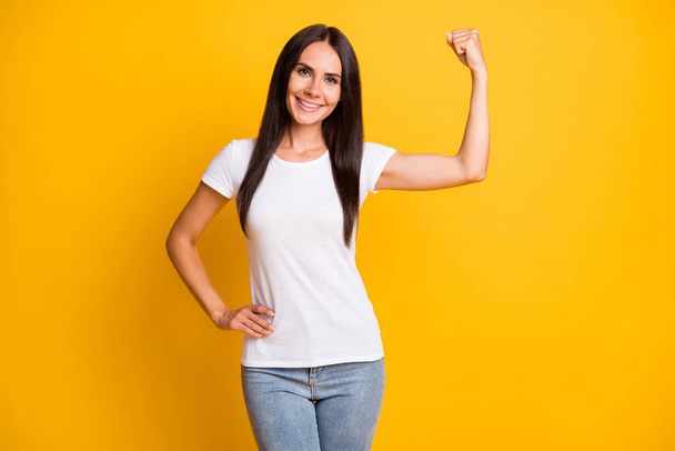 Photo portrait of brunette girl in stylish clothes showing strength triceps smiling isolated on vivid yellow color background - 写真・画像