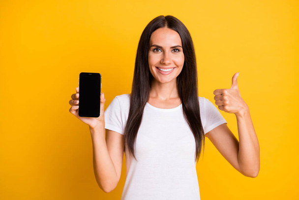 Photo of cute shiny young lady wear white t-shirt showing thumb up holding modern gadget isolated yellow color background - Фото, зображення