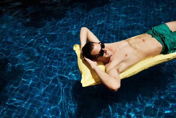 Tiro de um jovem relaxado flutuando em um lilo em uma piscina azul - Foto, Imagem