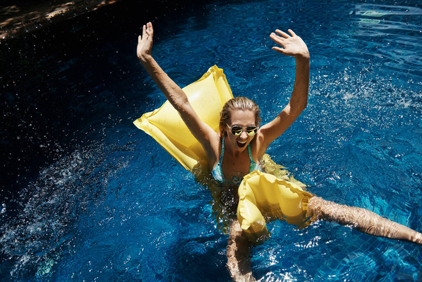 Tourné d'une jeune femme heureuse levant les mains en l'air alors qu'elle était assise sur une lilo dans la piscine - Photo, image