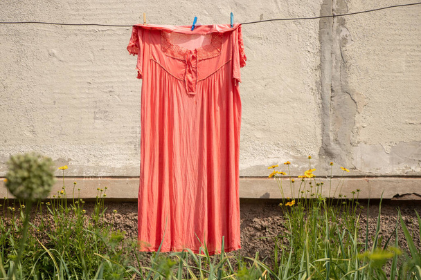 γυναικείο φόρεμα κρέμεται σε ένα σχοινί στο δρόμο στην αυλή κοντά στο σπίτι στεγνώνει στον ήλιο, πλένονται τα ρούχα σε ένα σχοινί - Φωτογραφία, εικόνα