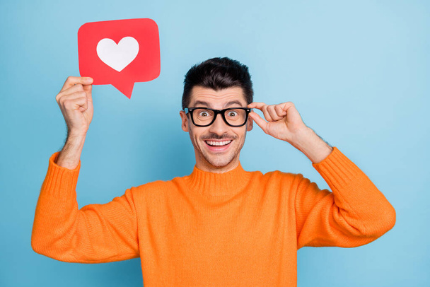 Photo of astonished cheerful person hold heart like paper card touch eyewear isolated on blue color background - Fotó, kép