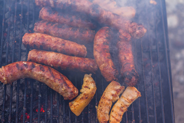 Grilling sausages on barbecue grill. Delicious sausages on charcoal grill - Фото, изображение