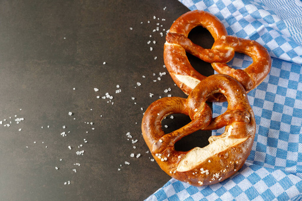 Traditional baked bavarian salty bread pretzels closeup with blue towel on brown rustic stone background. Top view with copy space - Photo, Image