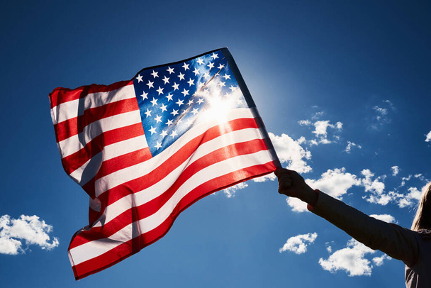 Mávání vlajkou USA v ruce proti modré obloze - Fotografie, Obrázek