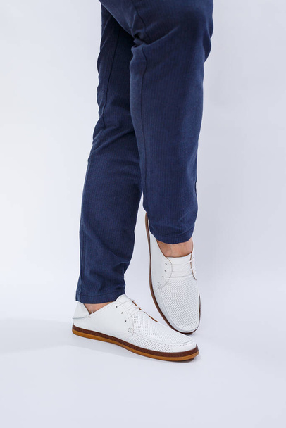 Men's feet in white everyday sneakers made of natural leather on lacing. High quality photo - Φωτογραφία, εικόνα