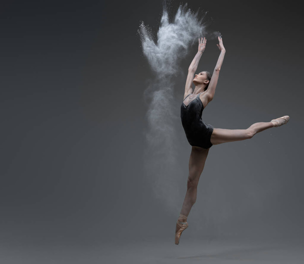 Skilled ballerina dancing leaping against gray background - Foto, imagen