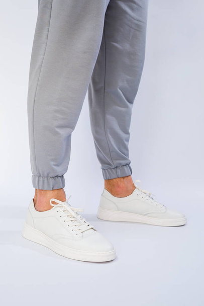 Męskie stopy w białych trampkach codziennego użytku wykonanych z naturalnej skóry na sznurowaniu. Wysokiej jakości zdjęcie - Zdjęcie, obraz