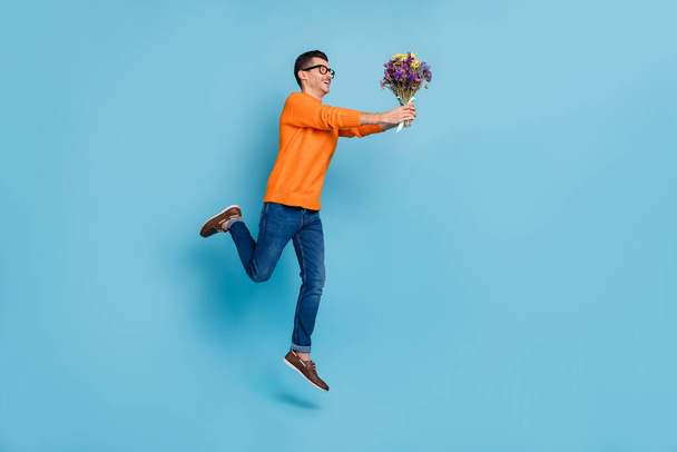 Full length profile portrait of cheerful man hurry fast hands hold flowers isolated on blue color background - Foto, afbeelding