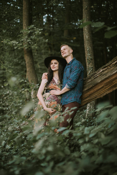 Pregnant girl with big cute belly and young man in beautiful forest - Фото, изображение