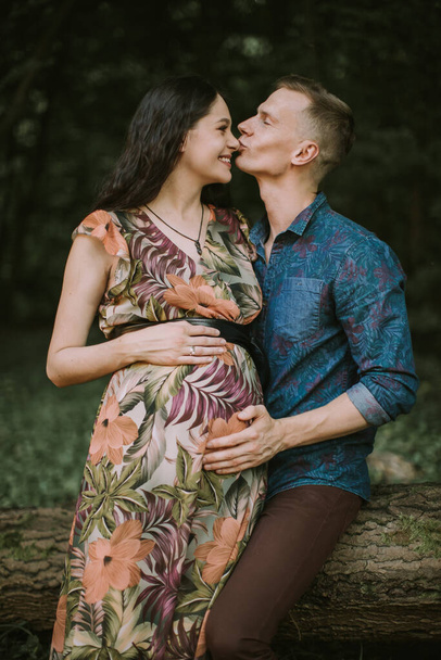 Beautiful young pregnant woman enjoying walk in nature with handsome husband, kissing her face - Foto, Bild