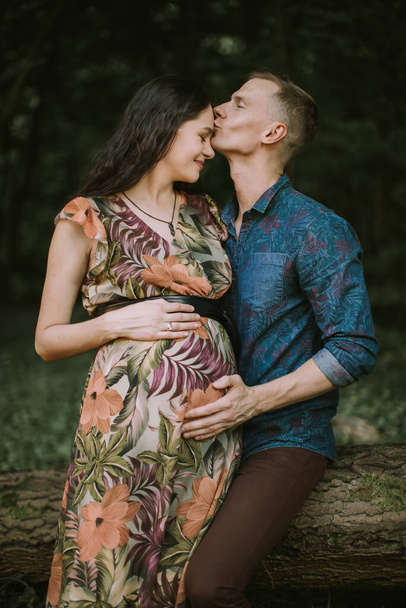 Beautiful young pregnant woman enjoying walk in nature with handsome husband, kissing her face - Photo, image