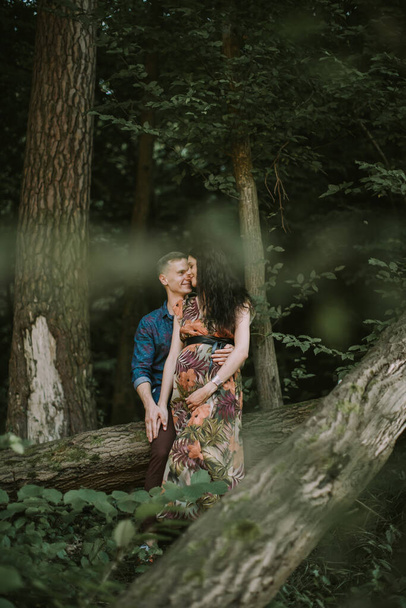 happy pregnant couple, standing in beautiful summer forest, hugging and smiling each other - Foto, Imagem