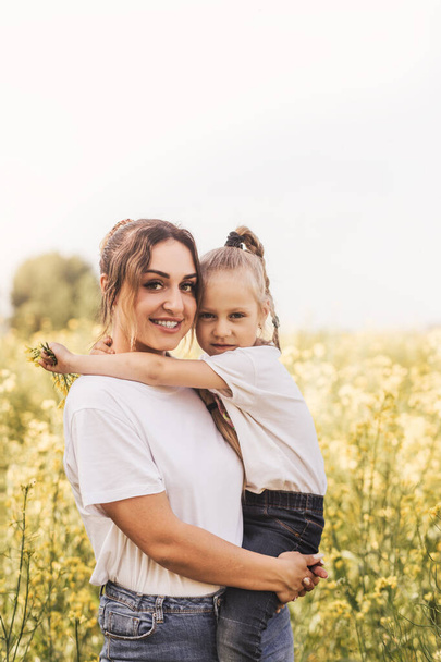 Mladá matka drží svou dceru v létě na kvetoucím poli. Krásná rodina a radost z mateřství. - Fotografie, Obrázek