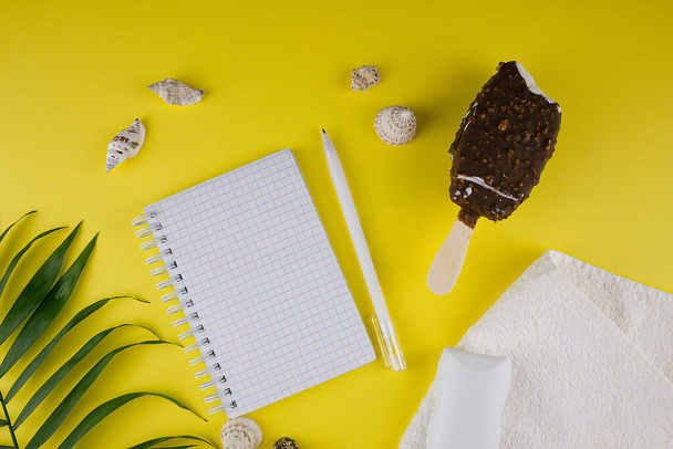 A template for vacation plans, shells, chocolate-coated ice cream, a white towel, a tube of sunscreen or sunscreen and a green palm leaf on a modern yellow background with a place to copy. - Foto, immagini