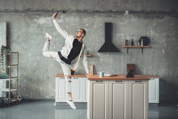 Jumping man is making a selfie in the kitchen while working from home on a tablet - Foto, Imagem