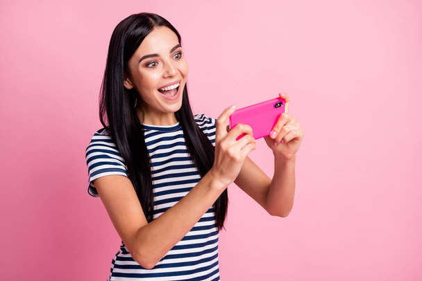 Photo portrait of woman playing video games holding phone in two hands vertically isolated on pastel pink colored background - Foto, immagini