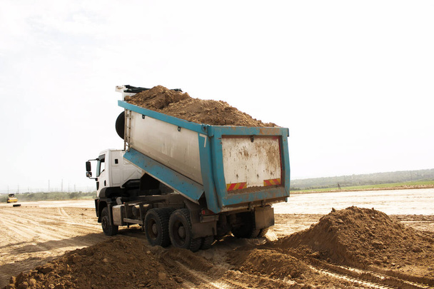 Το φορτηγό ξεφορτώνει χώμα από πηλό για την κατασκευή νέας εθνικής οδού. Πηλός για τη θεμελίωση νέου δρόμου. - Φωτογραφία, εικόνα