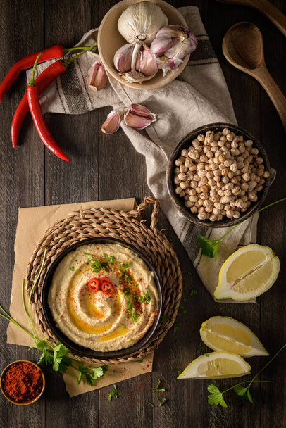 Delicious hummus in ceramic bowl. Colorful snack composition on a black wooden background. - Foto, imagen