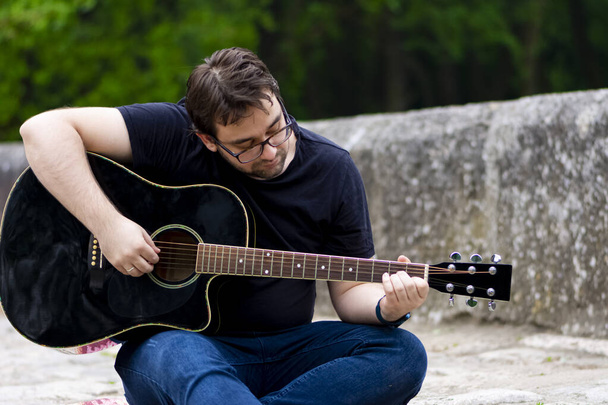Young man playing guitar sitting on the bridge - 写真・画像