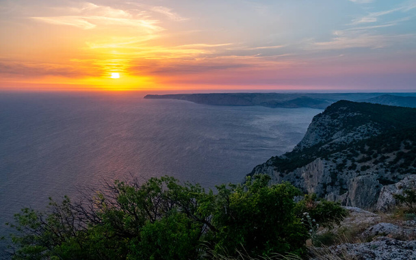 The sun setting into the sea and the long cape crashing into the Black Sea at sunset. Coast of the Crimean Peninsula near Balaklava. - Fotoğraf, Görsel
