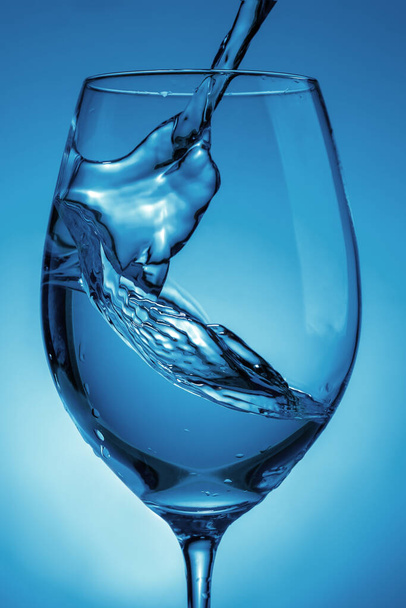 pouring water into a transparent glass for wine close-up. light blue background with water splashes - 写真・画像