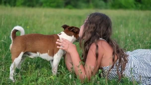 lindo poco caucásico chica mascota su perro acostado en la hierba - Imágenes, Vídeo