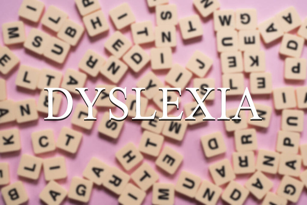 Blocos de azulejos alfabeto com palavra DYSLEXIA no centro em fundo rosa. Conceito de consciência da dislexia e desenvolvimento do cérebro humano - Foto, Imagem