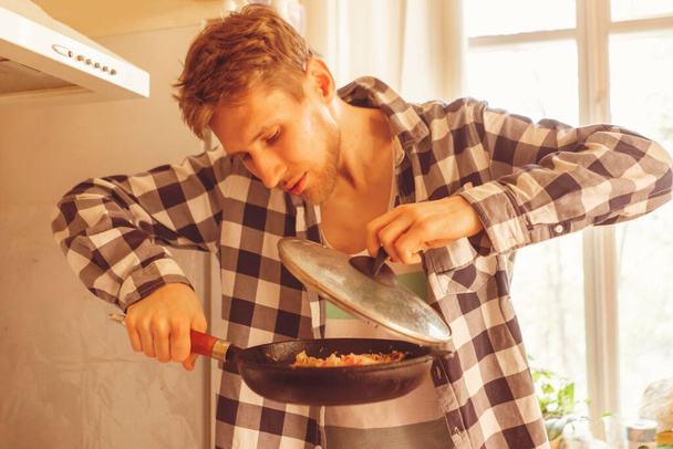 молодой человек готовит целительную еду на сковороде на кухне, приготовление пищи отдыха - Фото, изображение