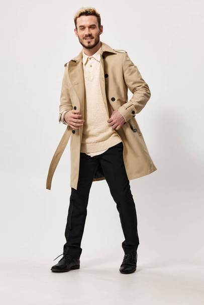 man in een beige jas met een riem in zijn hand en zwarte broek trui model - Foto, afbeelding