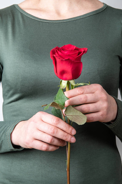 Beautiful woman in a green dress and holding one red rose - Фото, изображение