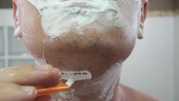 Uomo irriconoscibile schiuma da barba sul viso utilizzando rasoio di colore arancione - Filmati, video