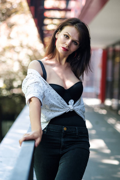 Eine attraktive reife Frau posiert in einer städtischen Umgebung. Sie trägt eine weiße Bluse und eine schwarze Korsage. - Foto, Bild