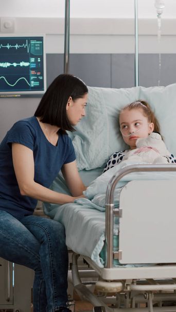 Занепокоєна мати сидить поруч з хворою дочкою під час огляду хвороби в лікарняному палаті
 - Фото, зображення