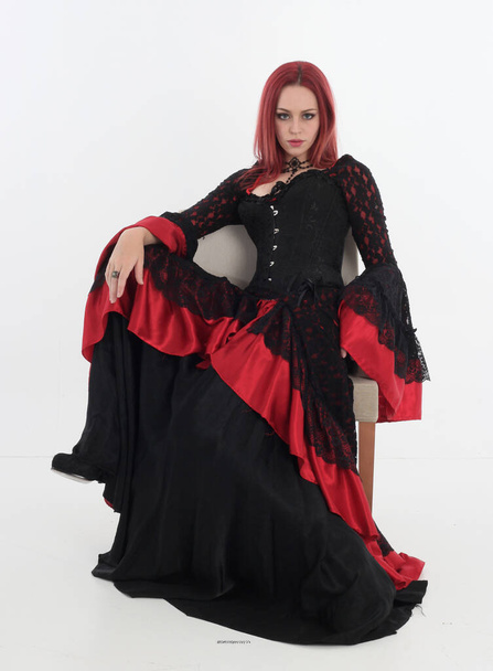 full length portrait of red haired woman wearing long black gothic victorian vampire gown. posing on white studio background. - Zdjęcie, obraz