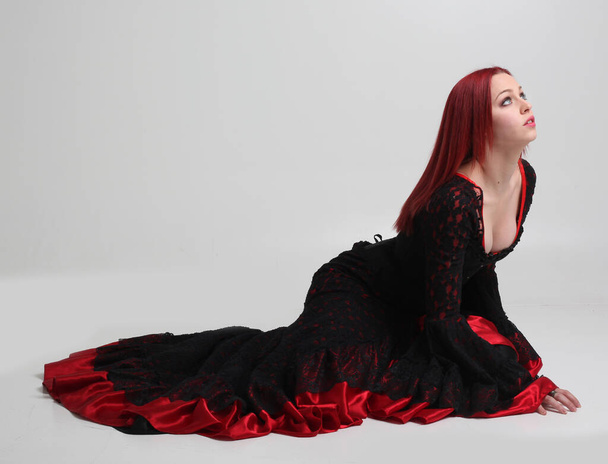 full length portrait of red haired woman wearing long black gothic victorian vampire gown. posing on white studio background. - Photo, image