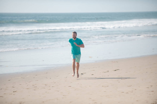 Morning jogging on a sandy beach near sea or ocean. Man running on beach. - Фото, изображение