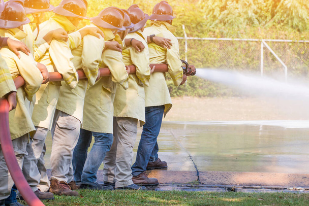 Palomiehet käyttävät sammutinta ja vettä letkusta palontorjuntaan vakuutusryhmän tulitaistelukoulutuksessa. Palomies yllään palopuku turvallisuuden vaaran koulutustapauksessa - Valokuva, kuva