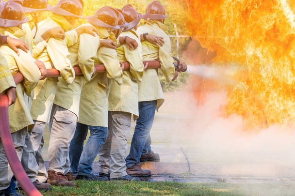 Hasiči používající vodu z hadice pro hašení požáru při protipožárním výcviku pojišťovací skupiny.Hasič v protipožárním skafandru pro bezpečnost pod nebezpečím výcvikového případu - Fotografie, Obrázek