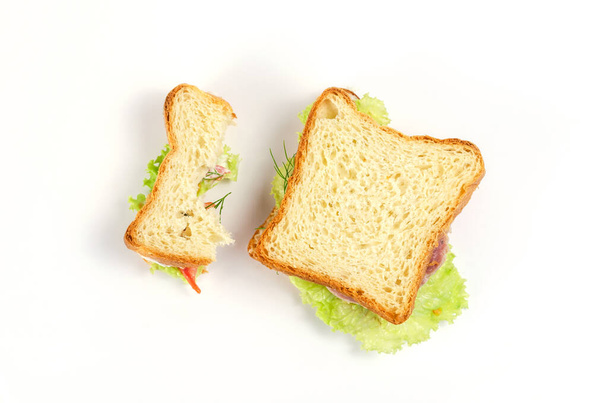Sanduíches de presunto em um fundo branco. Sanduíche de presunto meio comido e inteiro com presunto, tomate vermelho, alface verde, endro e molho de creme. Vista superior - Foto, Imagem
