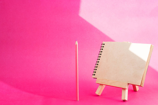 Empty notebook with craft texture pages. Spiral blank craft paper notebook on mini easel and pencil. Creative concept back to school. Stationery still life on bright pink background. - Foto, immagini