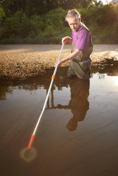 Water quality analyst dressed in chest wader collecting samples - Foto, Imagem