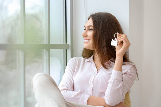 Ευτυχισμένη νεαρή γυναίκα με κλειδί από το σπίτι κοντά στο παράθυρο - Φωτογραφία, εικόνα
