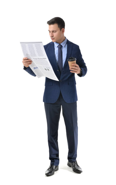 Young businessman with cup of coffee reading newspaper on white background - Photo, Image