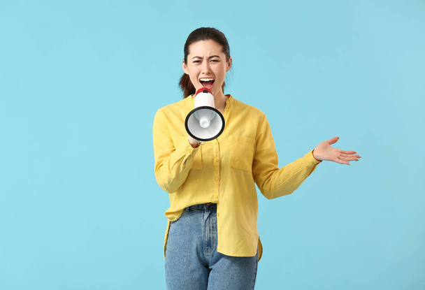 Angry young woman with megaphone on color background - Photo, Image