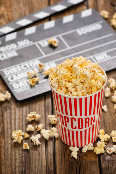 Bucket with tasty popcorn and movie clapper on wooden background, closeup - Photo, Image