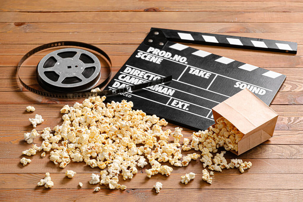Tasty popcorn with movie clapperboard and reel on wooden background - Fotó, kép